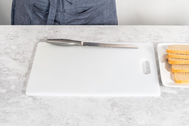 Cutting stale bread with a bread knife on a white cutting board to make croutons