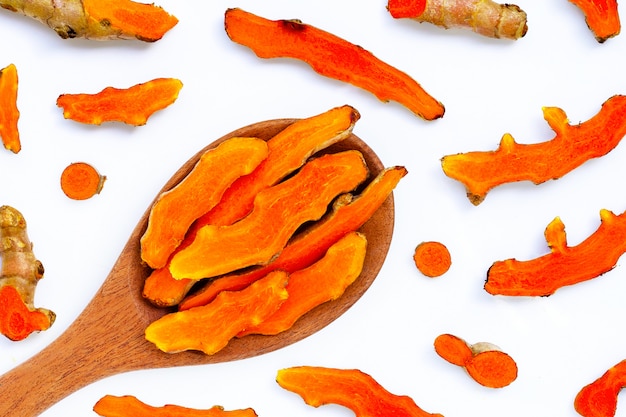 Cutting of turmeric roots on wooden spoon on white