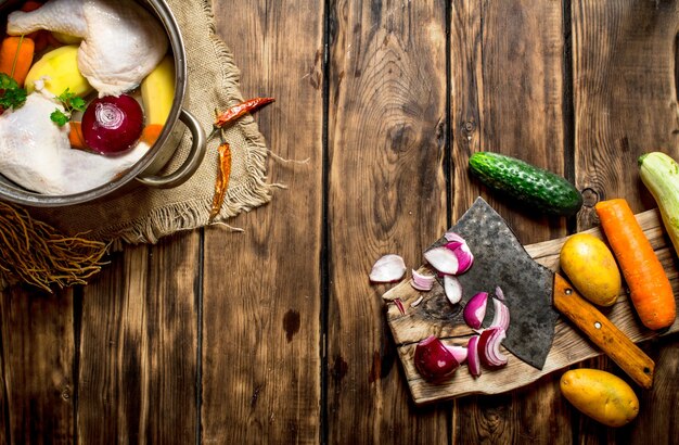 Cutting of vegetables to chicken broth on wooden table.