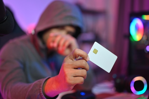Cyber crime and network security concept Mystery hacker in hoodie holding credit card in his hand