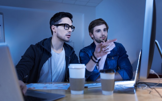 Cyber fraud. Smart intelligent handsome hacker pressing the button on the laptop keyboard and pointing at the commuter screen while showing how to hack a website