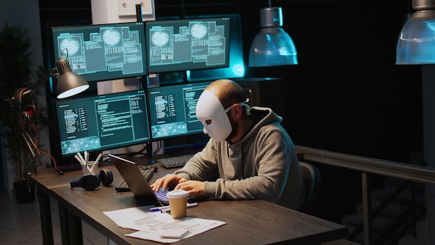 cyber impostor wearing mask hacking database servers, hacker with hood breaking into computer system and activating virus to create malware. mysterious impostor stealing big data. handheld shot.