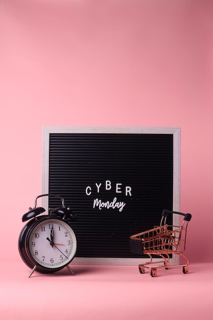 Cyber Monday on letter board, alarm clock and mini trolley isolated on pink background. 