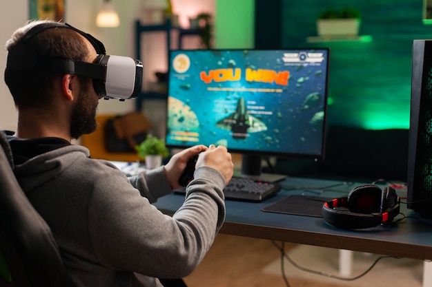 Cyber pro gamer winning online video game tournament wearing\
virtual reality headset. professional player using joypad for space\
shooter championship sitting on gamining chair playing on\
computer