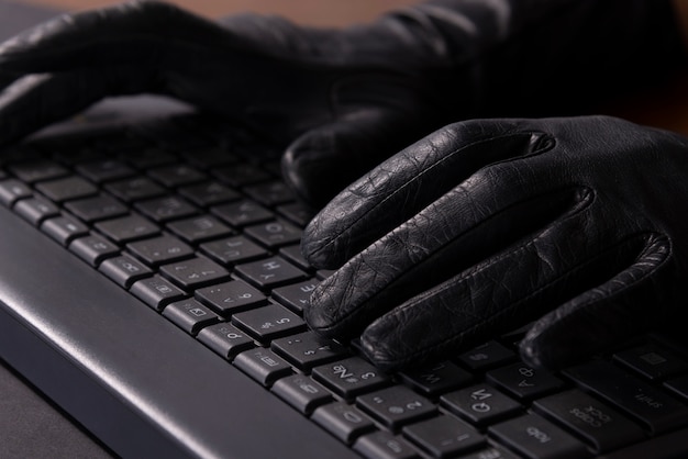 Киберпреступники руки в перчатках на клавиатуре ноутбука.