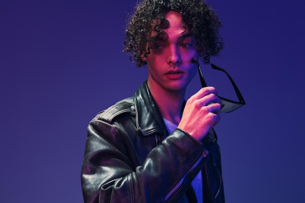 Cyberpunk stijl curly man lederen jas spiegel brillen kijkt opzij poseren geïsoleerd op kleur roze blauw studio achtergrond Cool mode aanbod enorme seizoensgebonden verkoop nieuwe collectie concept kopie ruimte advertentie