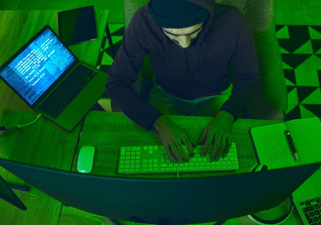 Foto crimine di sicurezza informatica e programmazione dell'uomo dall'alto in ufficio al neon con frode di codice e hacking software ransomware e web hacker su attacco informatico ladro di password codifica truffa online e computer