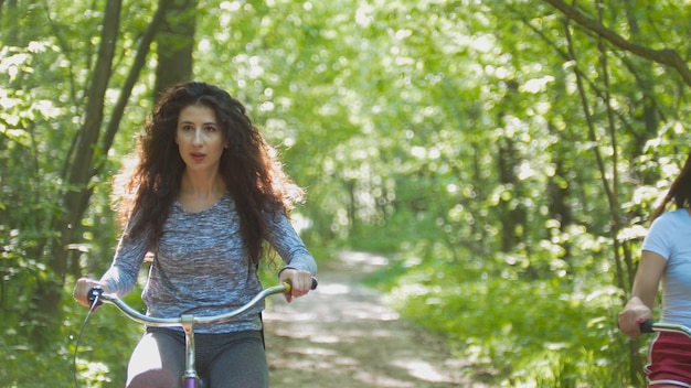 Брюнетка-велосипедистка едет на велосипеде на фоне зеленых деревьев Телефотосъемка солнечного дня