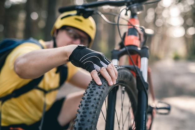 Cyclist checking bicycle tire pressure before ride in forest