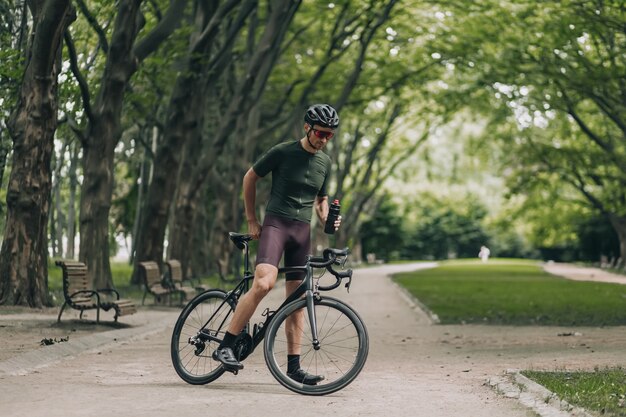 Cyclist in helmet and glasses drinking water at park