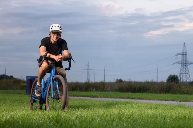 Cyclist in helmet and glasses stands with bike on the green grass in the park