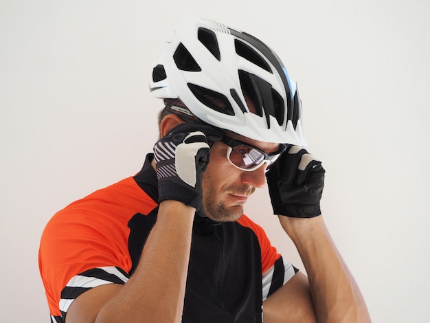 A cyclist in a jersey and helmet puts on sunglasses. Close up portrait.