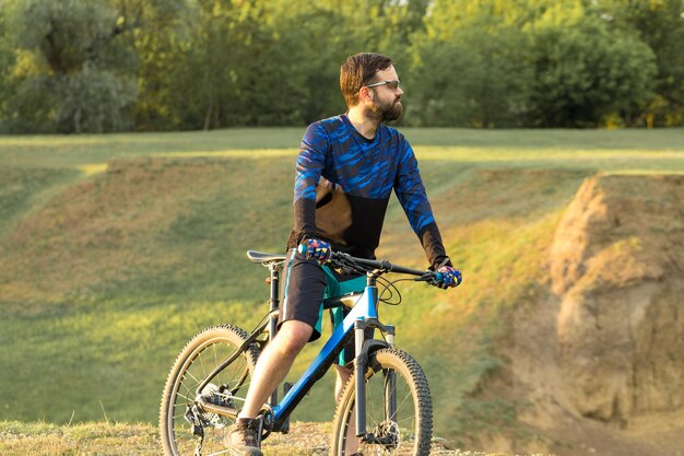 Cyclist in pants and fleece jacket on a modern carbon hardtail bike with an air suspension fork rides offroad The guy is resting on a bench in the autumn park