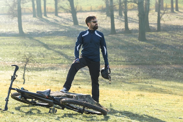 Cyclist in pants and fleece jacket on a modern carbon hardtail bike with an air suspension fork rides offroad The guy is resting on a stump in the park looks into the distance