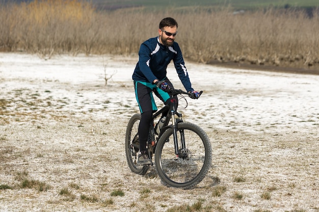 Велосипедист в штанах и флисовой куртке на современном карбоновом хардтейл-байке с пневмоподвеской.