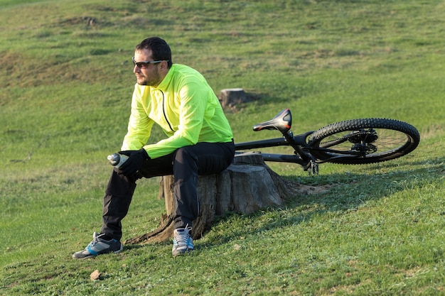 エアサスペンションフォークを備えたモダンなカーボンハードテールバイクのパンツとグリーンのジャケットを着たサイクリスト。丘の上の男は自転車に乗る。