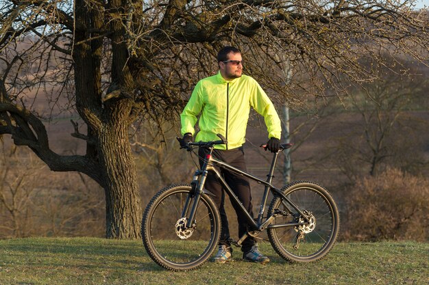 에어 서스펜션 포크가 있는 현대적인 탄소 하드테일 자전거에 바지와 녹색 재킷을 입은 사이클리스트