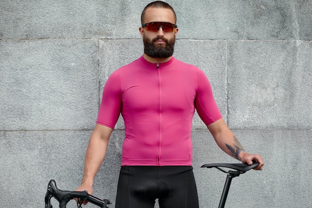 Photo cyclist in pink sportwear resting after an workout while standing against cement wall background with copy space area for text message or advertising