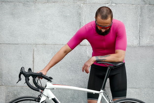 Ciclista in abbigliamento sportivo rosa che riposa dopo un allenamento in piedi sullo sfondo del muro di cemento con area di copia spazio per messaggi di testo o pubblicità