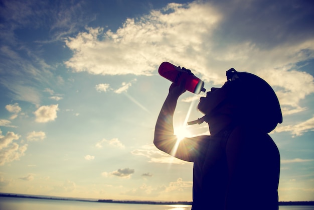 Siluetta di riciclaggio dell'acqua potabile e del ciclista al tramonto.