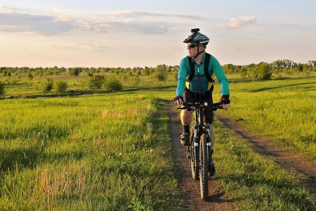 Cyclist rides on the road in a field on a bright sunny day
