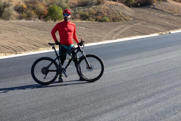 晴れた空を背景に道路で自転車に乗るサイクリスト 秋の晴れた日に自転車で立っている服装の男