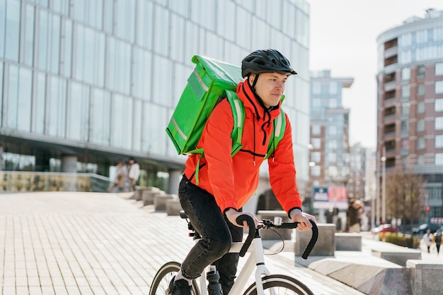 ランチやディナーの食べ物を届けるサーモバッグを持って自転車に乗るサイクリスト オフィスの男性宅配業者