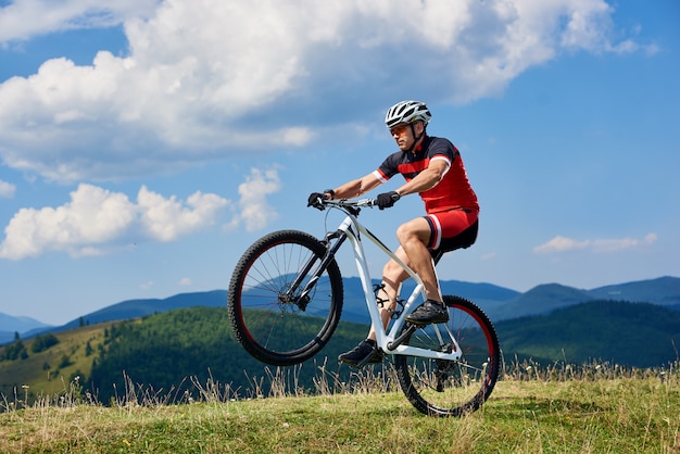 Cyclist riding cross country bike, turning on one wheel of bicycle on mountain hill