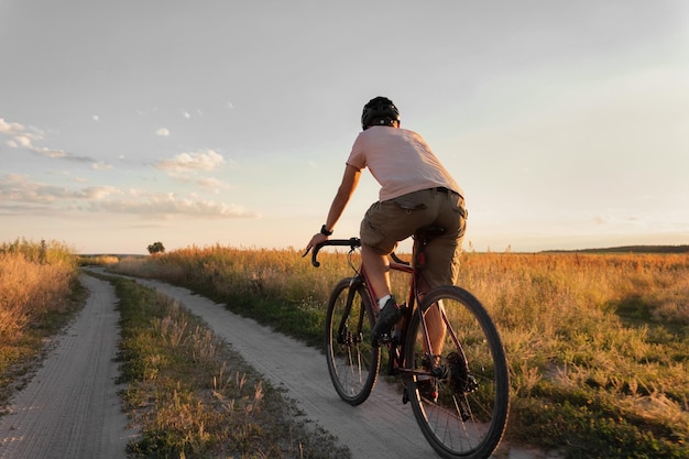 写真 夕暮れに砂利の自転車に乗って田舎の小道を走るサイクリスト 旅行とアクティブなライフスタイルのコンセプト