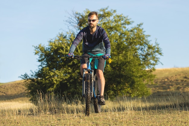 Cyclist in shorts and jersey on a modern carbon hardtail bike on a field background