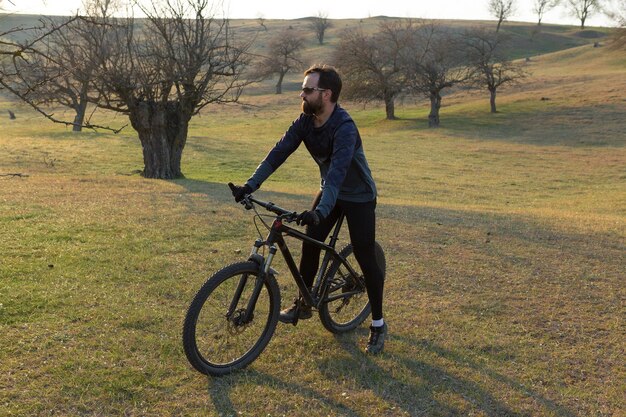 Cyclist in shorts and jersey on a modern carbon hardtail bike with an air suspension fork standing on a cliff against the background of fresh green spring forest