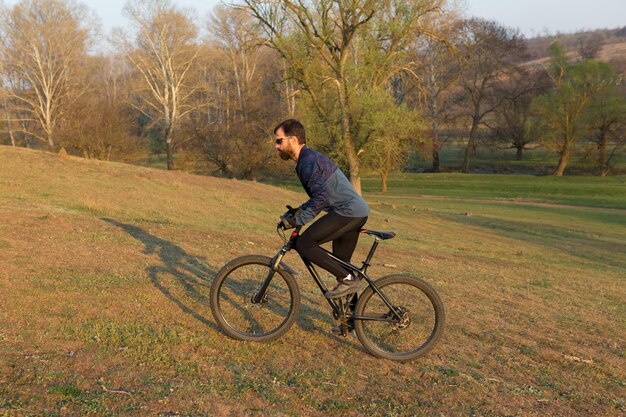 Cyclist in shorts and jersey on a modern carbon hardtail bike with an air suspension fork standing on a cliff against the background of fresh green spring forest