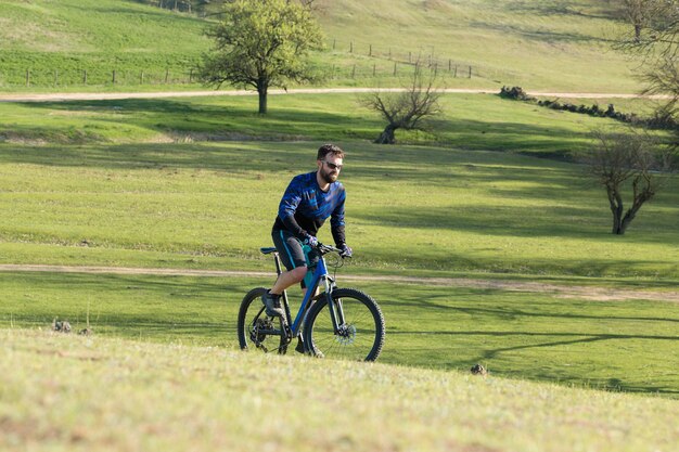 Cyclist in shorts and jersey on a modern carbon hardtail bike with an air suspension fork standing on a cliff against the background of fresh green spring forest