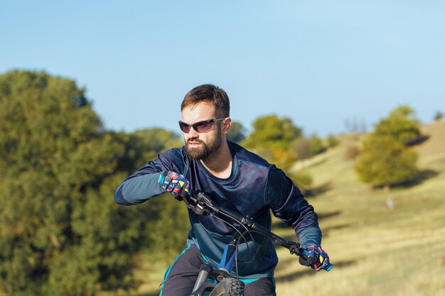 Cyclist in shorts and jersey on a modern carbon hardtail bike with an air suspension fork standing on a cliff against the background of fresh green spring forest