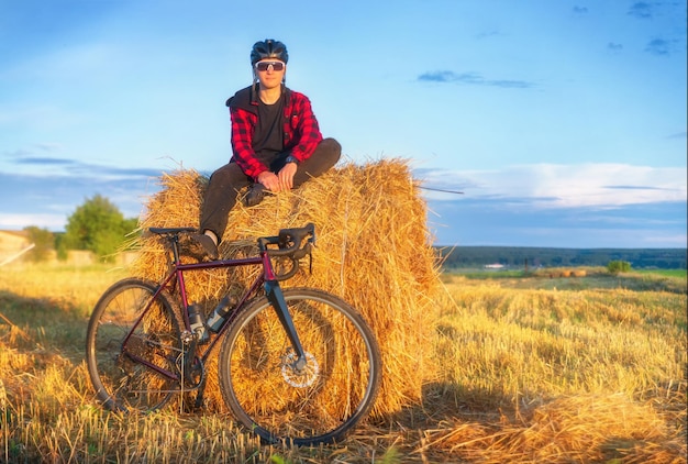 Cyclist sits on a haystack after a bike ride at sunset Active lifestyle and travel concept