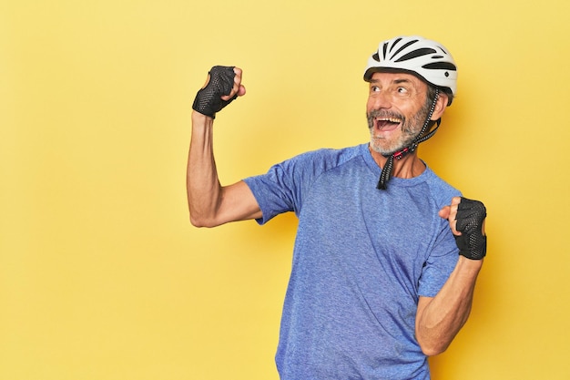 Cyclist wearing helmet in yellow studio raising fist after a victory winner concept