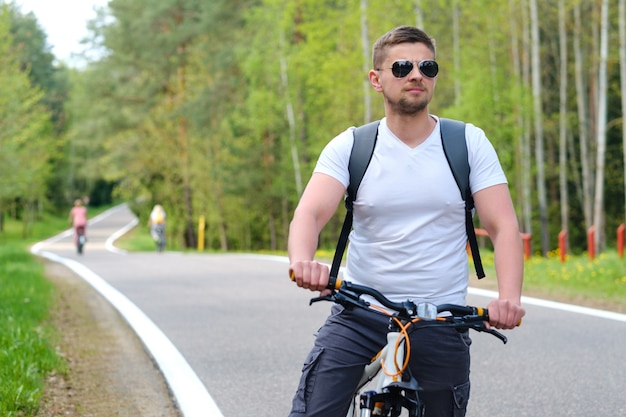 A cyclist with a backpack and glasses rides a bicycle on a forest road enjoying nature.