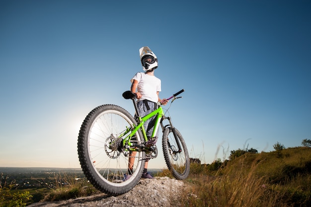 Ciclista con la mountain bike sulla collina sotto il cielo blu