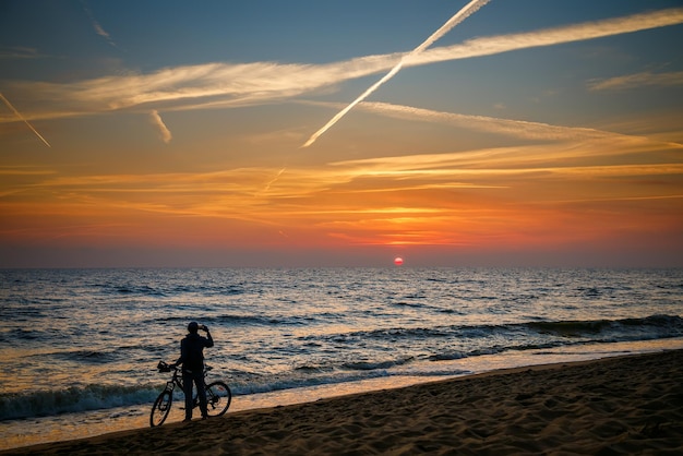 サイクリストの女性が海辺で立ち止まり、美しい夕日のスナップショットを撮った