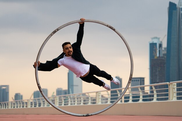 Artista di cyr wheel che indossa abiti eleganti in bianco e nero con il paesaggio urbano di dubai durante il tramonto.