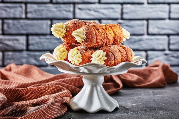 Czech kremrole: traditional pastry filled with buttercream frosting, served on a white cake stand in front of black brick wall