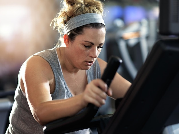 Daag jezelf uit en blijf doorgaan Shot van een vastberaden ogende vrouw die aan het trainen is op een elliptische machine in de sportschool