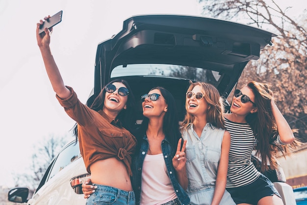 Daarom maken wij roadtrips! Vier mooie jonge vrolijke vrouwen die selfie maken met een glimlach