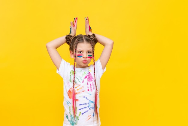 A dabbling girl stained in paints shows horns on a yellow isolated background The child is playing with colorful paints Courses for the development of children's creativity Happy childhood games