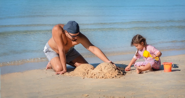 아빠와 딸이 해변에 모래성을 짓고 있습니다. 남자는 바다에 의해 그의 딸과 함께 재생