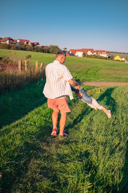 写真 太陽が沈む夏の晴れた日に草原で歩いている白人の外見の父と娘 娘と一緒に自然の中で遊んでいる男