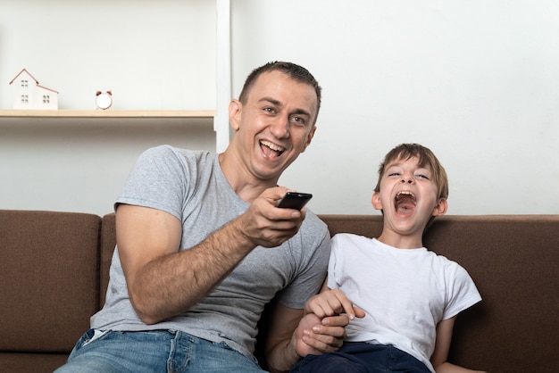Папа и сын смотрят телевизор и громко смеются. семейные отношения.