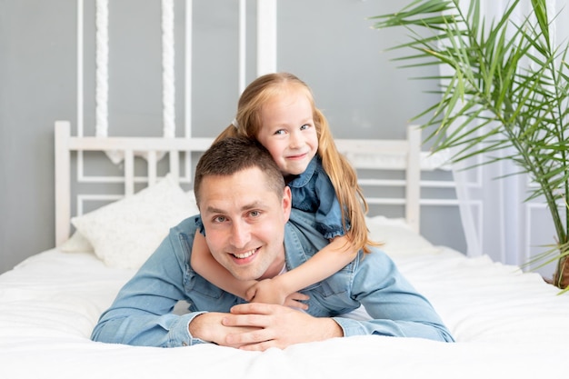 Dad and baby daughter have fun playing and cuddling at home on the bed