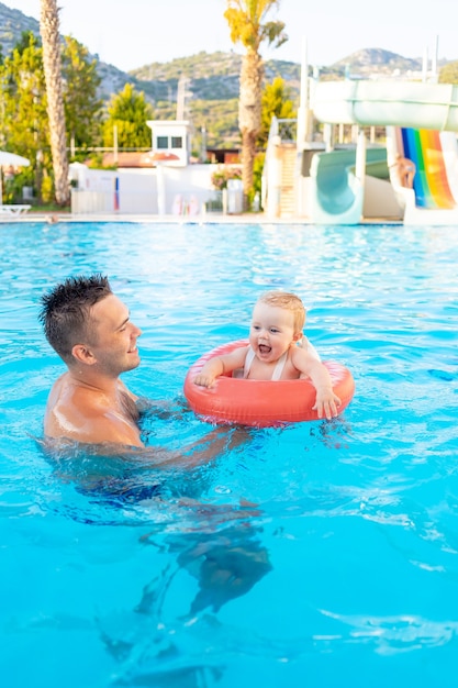 여름에는 워터 슬라이드가 있는 수영장에서 부풀릴 수 있는 원 안에 있는 아빠와 아기는 가족과 함께 즐거운 수영, 휴식을 취하고 시간을 보냅니다.