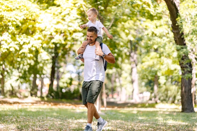 Dad carries the child on his shoulders while they fool around on a sunny day in the park